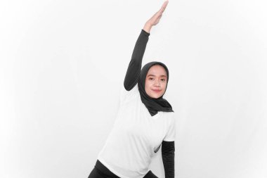 Başörtüsü takan beyaz elbiseli kadınların jimnastik hareketleri bir elini kaldırıyor.