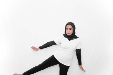 Beyaz elbiseli tesettür giyen bir kadın jimnastik yapar, kolları yana doğru açılır, bacakları yana doğru kalkar..