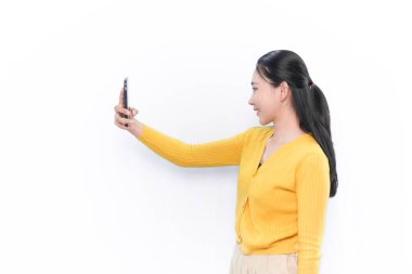 Sarı elbiseli Endonezyalı kadın akıllı telefonlu selfie çekiyor.