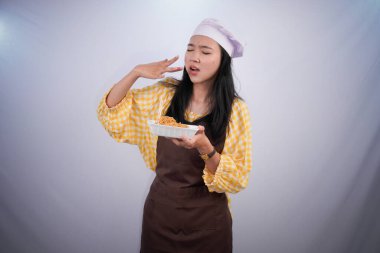 Şef üniformalı Asyalı kadın elinde erişte ve baharat kabı tutuyor.