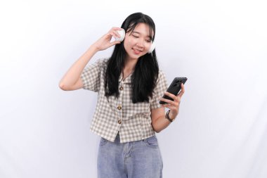 Beyaz kareli gömlek giyen Asyalı kadın müzik dinliyor ve akıllı telefon çalıyor.