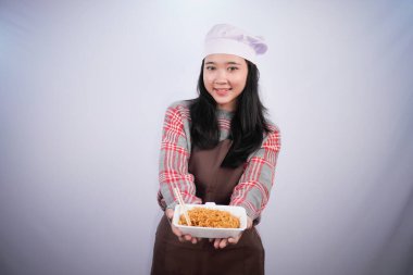 Şef üniforması giyen Endonezyalı kadın konteynırda kızarmış şehriye gösteriyor.