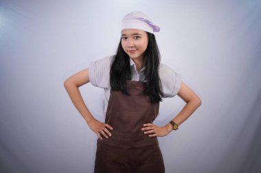 Aşçı üniformalı Endonezyalı kadın gülümsüyor ve ellerini kalçalarına koyuyor.