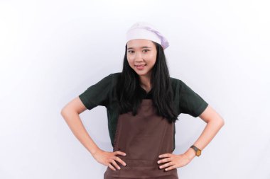 Asyalı Endonezyalı kadın şef üniforması giyiyor gülümsüyor ve ellerini kalçalarına koyuyor.