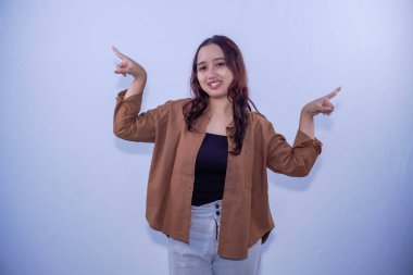 Kahverengi elbiseli Endonezyalı kadın gülümsüyor ve sağa sola işaret ediyor.