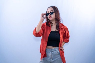 Endonezyalı turuncu elbiseli, güneş gözlüğü takan, tek eli kalçasında Asyalı bir kadın.