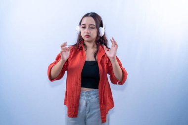 Turuncu elbiseli Endonezyalı kadın kulaklık takıyor ve müzik dinliyor.