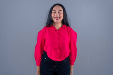 Asyalı Endonezyalı kadın kırmızı elbiseler giyiyor gözlerini kapatıyor ve dilini dışarı çıkarıyor.