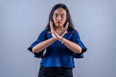 Endonezyalı Asyalı kadın uzun kollu mavi bir gömlek giyiyor ve bir anlaşmazlık işareti veriyor.