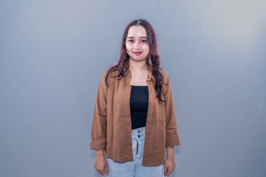 Kahverengi elbiseli Endonezyalı kadın gülümsüyor ve dimdik duruyor.