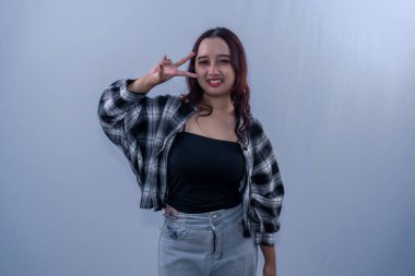 Siyah kareli elbiseli Endonezyalı kadın iki parmağıyla gülümsüyor.