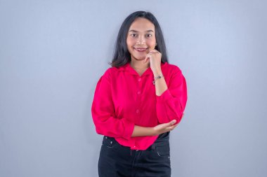 Asyalı Endonezyalı kadın kırmızı elbise giyiyor, gülümsüyor ve elleriyle yanağa dokunuyor.