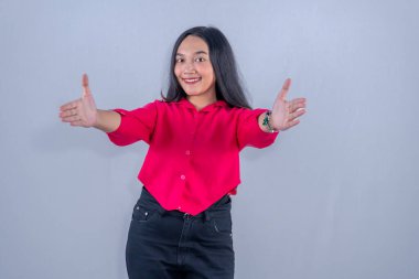 Kırmızı elbiseli Asyalı kadın gülümsüyor ve iki elini de açıyor.