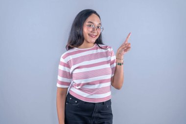 Beyaz tişörtlü, pembe çizgili, gülümseyen ve yukarı bakan Asyalı kadın.