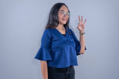 Mavi elbiseli Endonezyalı kadın gülümsüyor ve tamam işareti veriyor.