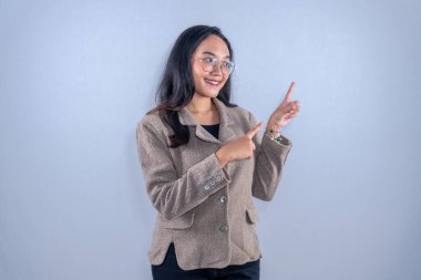 Kahverengi ceket giyen Asyalı kadın gülümsüyor ve yan tarafı işaret ediyor.