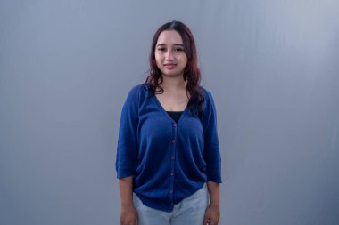 Asyalı Endonezyalı kadın mavi elbiseli, dik duruyor ve gülümsüyor.