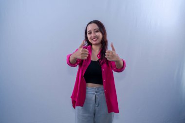 Asyalı Endonezyalı kadın kırmızı elbise giyiyor, gülümsüyor ve başparmağını kaldırıyor.