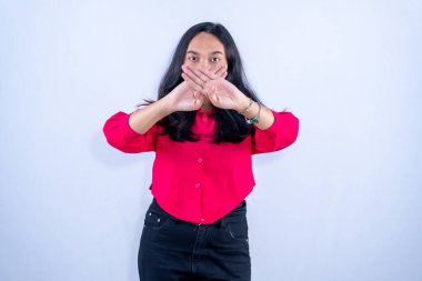 Kırmızı gömlekli bir kadın, elleri ağzının önünde çapraz durarak ya sessizlik işareti verir ya da konuşmayı reddeder..