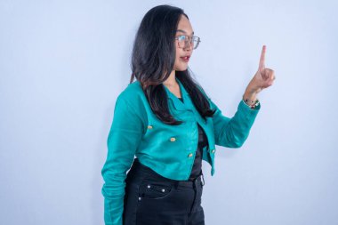 Gözlük ve deniz mavisi ceket takan kendine güvenen bir kadın işaret parmağıyla yukarı bakıyor. Bir fikir veya talimat öneriyor..