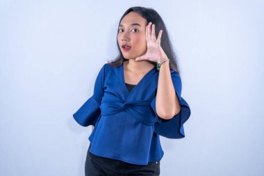 Mavi bluzlu genç bir kadın. Şaşırmış bir ifadeyle poz veriyor. Elini şakacı bir şekilde yüzüne yaklaştırıyor..