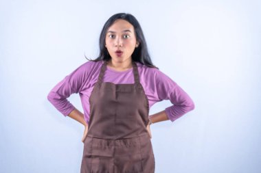 Mor gömlekli ve kahverengi önlüklü, elleri kalçasında, gözleri açık, şaşırmış bir Asyalı kadın..