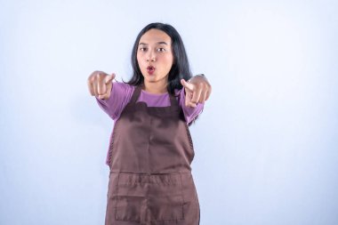 Mor gömlekli ve önlüklü genç bir Asyalı kadın her iki işaret parmağıyla öne bakıyor..