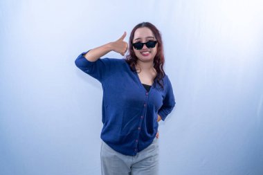 Endonezyalı Asyalı kadın mavi hırka giyiyor ve güneş gözlüğü takıyor gülümsüyor.