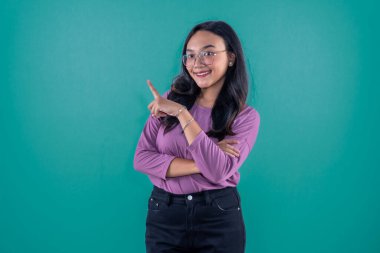 Mor elbiseli Endonezyalı kadın gülümsüyor ve yan tarafı işaret ediyor.