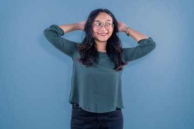 Endonezyalı, mavi elbiseli, gülümseyen ve başını iki eliyle tutan bir kadın.