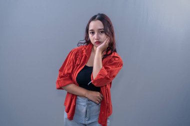 Turuncu gömlek giyen Asyalı bir Endonezyalı kadın dalgın ve çenesini tutuyor.