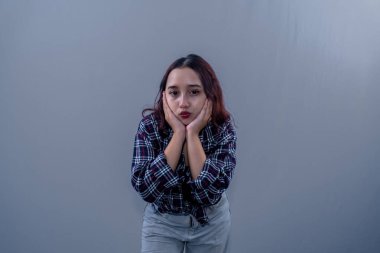 Endonezyalı Asyalı kadın siyah bir kareli gömlek giyiyor dudaklarını büzüyor ve çenesini tutuyor.