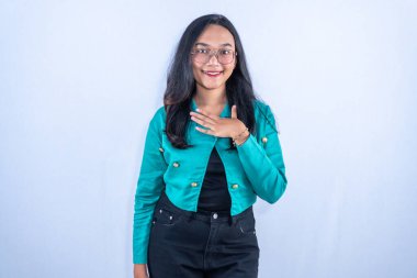 Endonezyalı, turkuaz elbiseli, göğsünü tutarken gülümseyen gözlüklü Asyalı kadın.