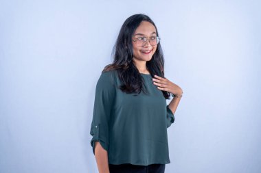 Asyalı Endonezyalı kadın mavi gömlek, gözlük takıyor, gülümsüyor ve göğsünü tutuyor.