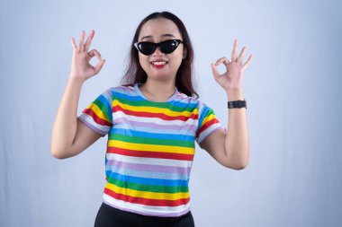 Endonezyalı siyah gökkuşağı renkli elbiseli, güneş gözlüklü, tamam işareti veren Asyalı kadın.