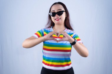 Siyah gökkuşağı giysili, güneş gözlüklü Endonezyalı kadın aşk işareti yapıyor.