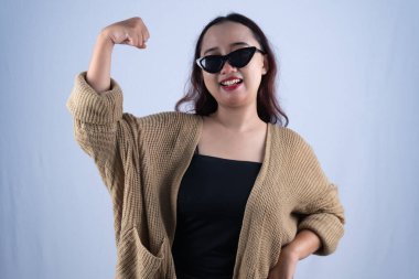 Kahverengi örgü hırka ve güneş gözlüğü takan Endonezyalı kadın gülümsüyor.