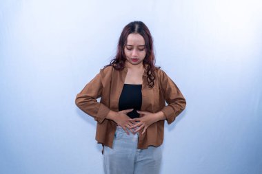 Kahverengi elbiseli Endonezyalı kadın karnını tutuyor çünkü erken hamilelik geçiriyor.