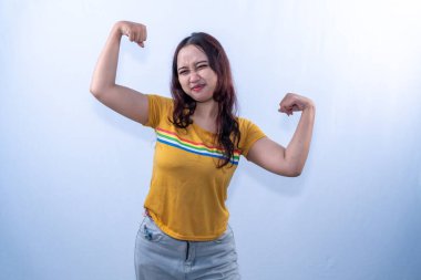 Sarı tişörtlü Endonezyalı kadın gülümsüyor ve güçlü bir işaret gösteriyor.