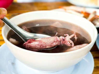 Kalamar mürekkep çorbası, beyaz tabakta metal kaşık ve ahşap masa. Thai lezzetli deniz ürünleri.