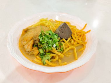 Kuzey Tayland usulü körili şehriye çorbası ve masada beyaz bir kase içinde tavuk. Khao Soi Tarifi. 