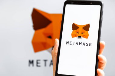 Ukrayna, Odessa - 9 Ekim 2021: MetaMaske uygulaması arka planda MetaMask logosuyla akıllı telefon ekranında çalışan el ele tutuşma uygulaması. MetaMaske yazılım şifreleme cüzdanıdır