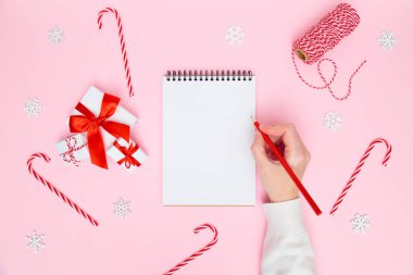 Noel arkaplanı. Kadın el yazısı boş deftere, şenlikli süslemeler, pastel pembeye hediye kutuları. Yeni yıl planlama, hedefler, yapılacaklar listesi veya dilek listesi konsepti. Düz yat, boşluğu kopyala