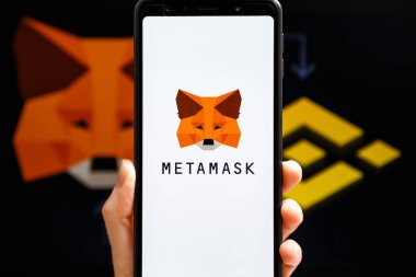 Ukrayna, Odessa - 9 Ekim 2021: MetaMaske uygulaması arka planda MetaMaske ve Binance logosu ile akıllı telefon ekranında çalışan el ele tutuşma uygulaması. MetaMaske Binance Akıllı Zincir kavramına bağlanıyor