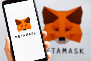 Ukrayna, Odessa - 9 Ekim 2021: MetaMaske uygulaması arka planda MetaMask logosuyla akıllı telefon ekranında çalışan el ele tutuşma uygulaması. MetaMaske yazılım şifreleme cüzdanıdır