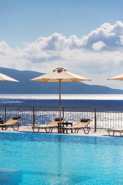 Luxury swimming pool with empty deck chairs and umbrellas at the resort with beautiful sea view.