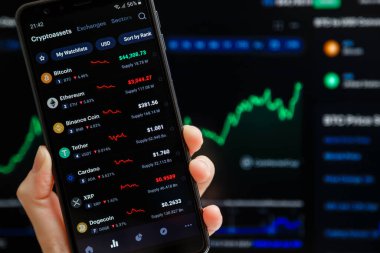 Ukrayna, Odessa - Ekim 9, 2021: Akıllı telefon ekranında çalışan CoinMarketCap uygulaması ile el ele tutuşmalar, günümüzün kripto para birimi fiyatlarının listesi, arka planda şamdan satışı