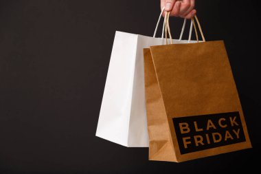 Kara Cuma indirimi. Elinde siyah arka planda Kara Cuma mesajı olan iki alışveriş çantası var. İndirim, alışveriş ve ekoloji kavramı