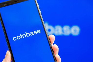Ukrayna, Odessa - 9 Ekim 2021: Arkaplanda Para Üssü logosu olan akıllı telefon ekranında çalışan Coinbase uygulaması ile el ele tutuşma cep telefonu. Para tabanlı Amerikan kripto döviz ve ticaret platformu
