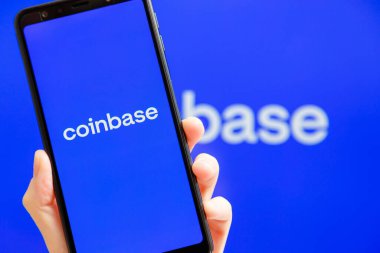 Ukrayna, Odessa - 9 Ekim 2021: Arkaplanda Para Üssü logosu olan akıllı telefon ekranında çalışan Coinbase uygulaması ile el ele tutuşma cep telefonu. Para tabanlı Amerikan kripto döviz ve ticaret platformu